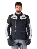 Man draagt een Alpinestars Bogotá Pro Drystar® Jas, Black Ice Gray en Yellow Fluo, all-season adventure touring motorjas, waterdicht ontwerp met meerdere zakken en verticale branding, gecombineerd met zwarte handschoenen en een grijze motorbroek