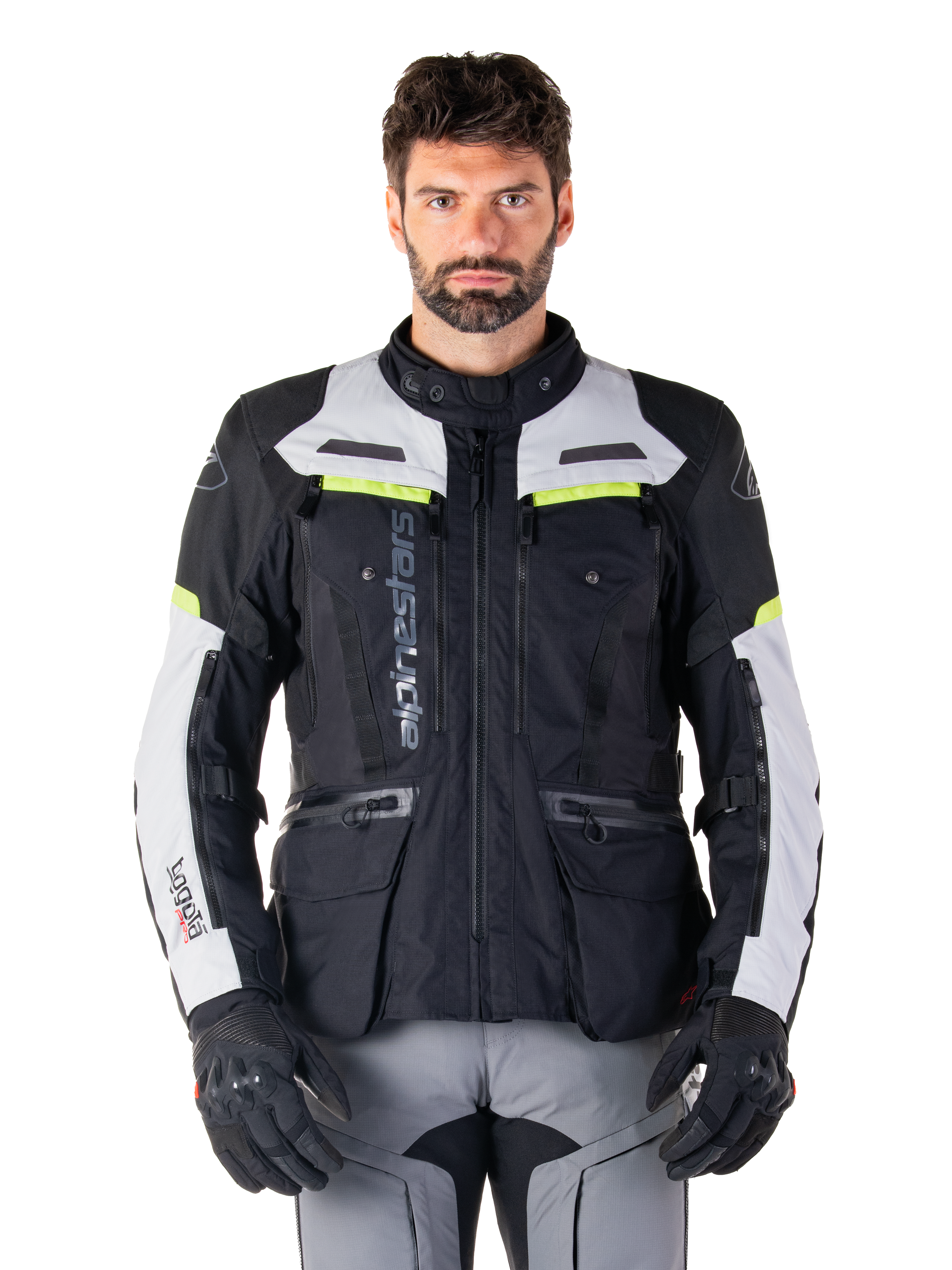 Man draagt een Alpinestars Bogotá Pro Drystar® Jas, Black Ice Gray en Yellow Fluo, all-season adventure touring motorjas, waterdicht ontwerp met meerdere zakken en verticale branding, gecombineerd met zwarte handschoenen en een grijze motorbroek