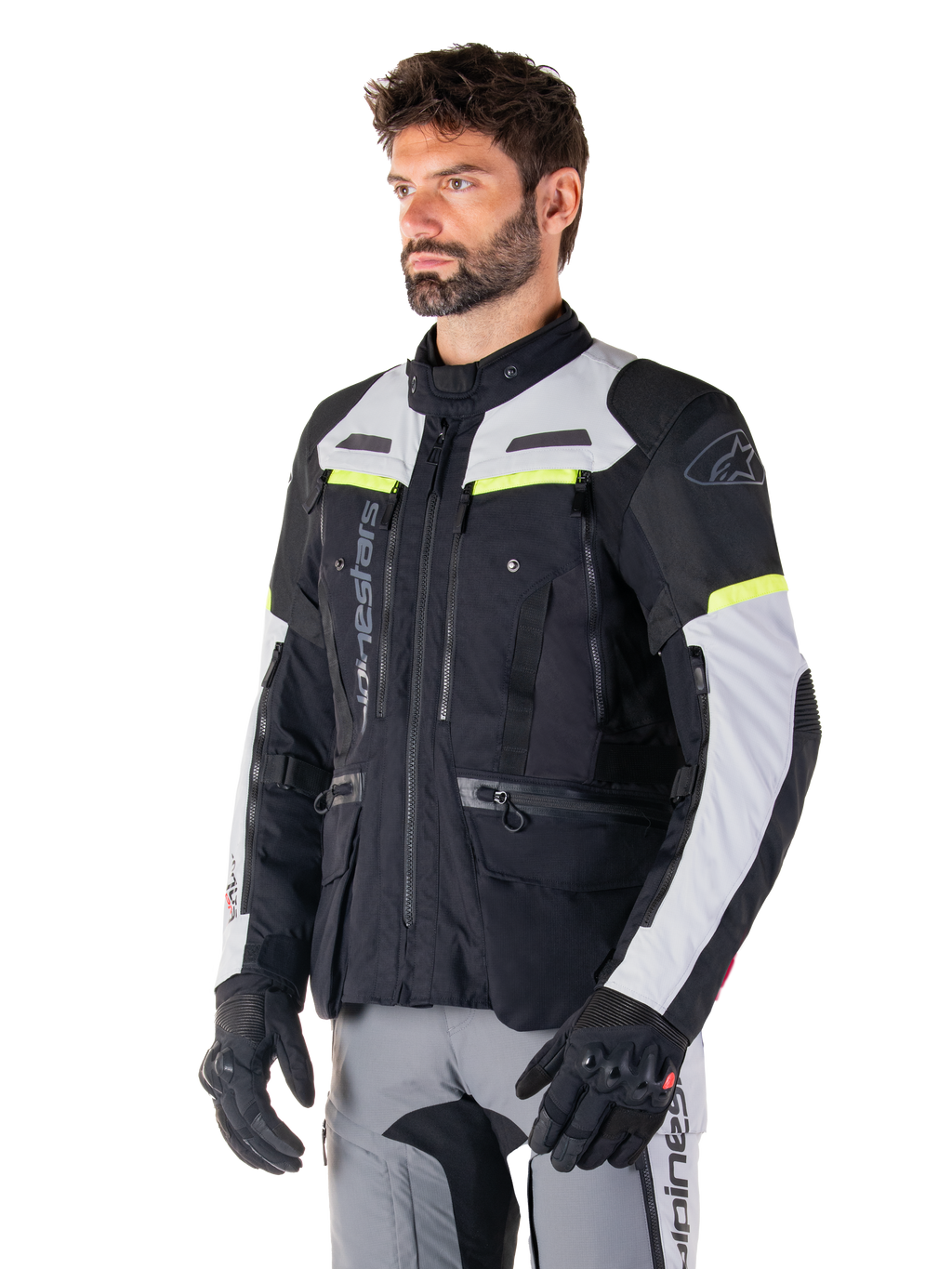 Alpinestars Bogotá Pro Drystar® Jas, adventure touring motorjas, Black Ice Gray en Yellow Fluo, gedragen door een man met bijpassende grijze broek en zwarte handschoenen, voorzien van technische ventilatiepanelen en een ontwerp met meerdere zakken.