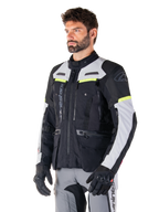 Alpinestars Bogotá Pro Drystar® Jas, adventure touring motorjas, Black Ice Gray en Yellow Fluo, gedragen door een man met bijpassende grijze broek en zwarte handschoenen, voorzien van technische ventilatiepanelen en een ontwerp met meerdere zakken.