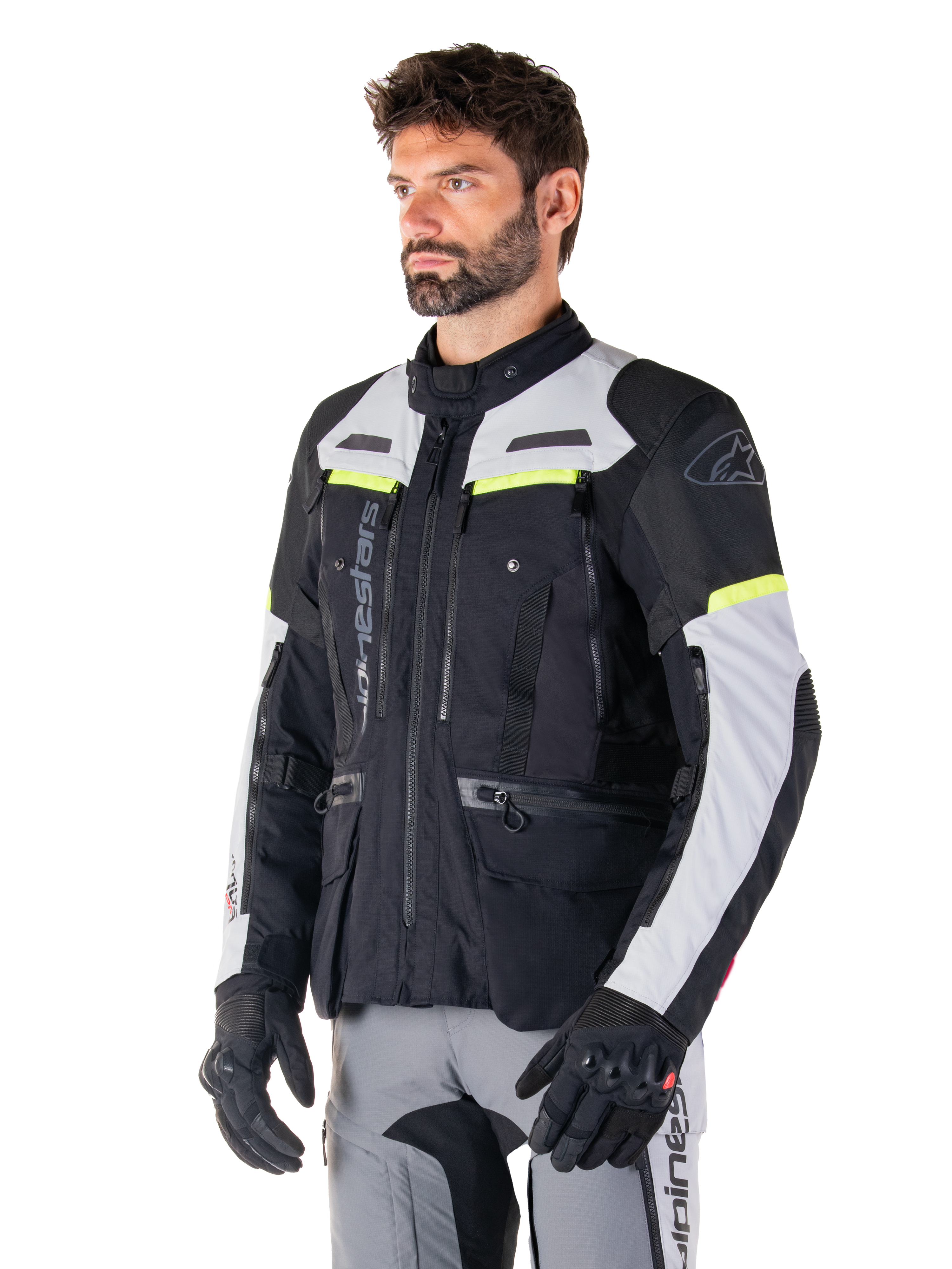 Alpinestars Bogotá Pro Drystar® Jas, adventure touring motorjas, Black Ice Gray en Yellow Fluo, gedragen door een man met bijpassende grijze broek en zwarte handschoenen, voorzien van technische ventilatiepanelen en een ontwerp met meerdere zakken.