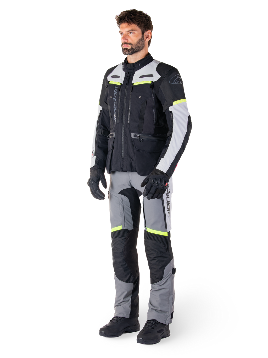 Alpinestars Bogotá Pro Drystar® Jas, adventure touring motorjas, Black Ice Gray Yellow Fluo, gedragen door model met bijpassende broek en zwarte handschoenen, met waterdichte textielconstructie, ventilatiepanelen en fluorescerende accenten.