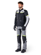 Alpinestars Bogotá Pro Drystar® Jas, adventure touring motorjas, Black Ice Gray Yellow Fluo, gedragen door model met bijpassende broek en zwarte handschoenen, met waterdichte textielconstructie, ventilatiepanelen en fluorescerende accenten.