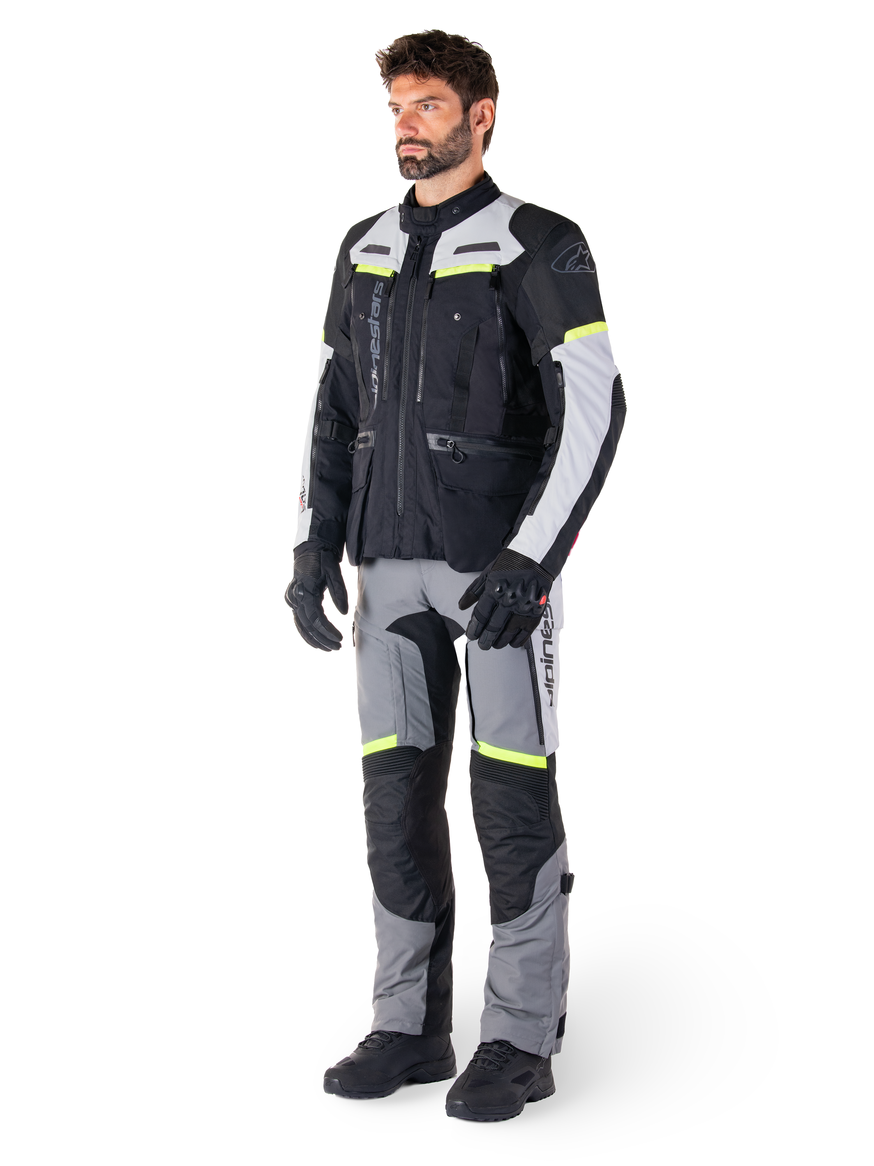 Alpinestars Bogotá Pro Drystar® Jas, adventure touring motorjas, Black Ice Gray Yellow Fluo, gedragen door model met bijpassende broek en zwarte handschoenen, met waterdichte textielconstructie, ventilatiepanelen en fluorescerende accenten.