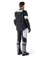 Achteraanzicht van een motorrijder die de Alpinestars Bogotá Pro Drystar® Jas in Black Ice Gray Yellow Fluo draagt, gecombineerd met bijpassende adventure touring broek, voorzien van een grote achterzak en fluorescerend gele accenten, all-season textiele motorkleding.