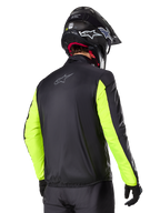 Alpinestars Bogotá Pro Drystar® Jas, achteraanzicht, zwart met Yellow Fluo mouwen, gedragen door een rijder met zwarte helm en handschoenen, high-visibility adventure touring motoruitrusting met een technische textielafwerking.