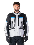Alpinestars Bogota Pro Drystar jas, adventure touring motorjas, Ice Gray met zwarte en cyaanblauwe accenten, vooraanzicht met ventilatiepanelen en cargozakken, gedragen door een model met zwarte motorbroek en handschoenen