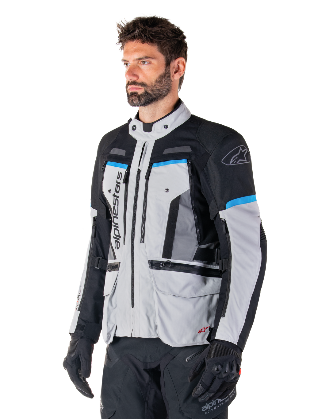 Alpinestars Bogota' Pro Drystar® Jas, Ice Gray, zwart en cyaan, adventure motorjas gedragen door een man met zwarte handschoenen, technisch ontwerp met meerdere zakken en ventilatiepanelen, hoogwaardige motoruitrusting