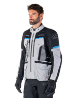 Alpinestars Bogota' Pro Drystar® Jas, Ice Gray, zwart en cyaan, adventure motorjas gedragen door een man met zwarte handschoenen, technisch ontwerp met meerdere zakken en ventilatiepanelen, hoogwaardige motoruitrusting
