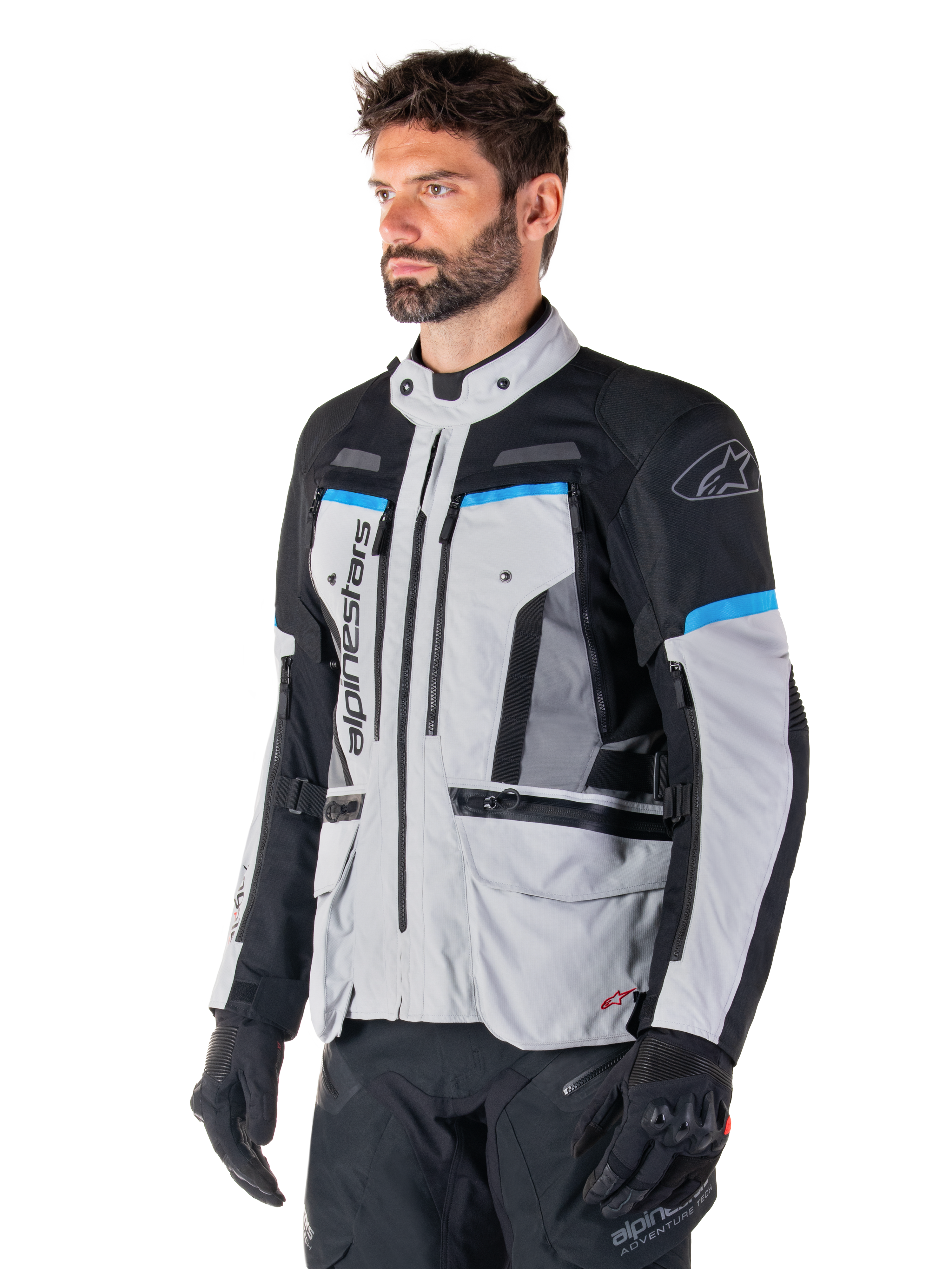 Alpinestars Bogota' Pro Drystar® Jas, Ice Gray, zwart en cyaan, adventure motorjas gedragen door een man met zwarte handschoenen, technisch ontwerp met meerdere zakken en ventilatiepanelen, hoogwaardige motoruitrusting