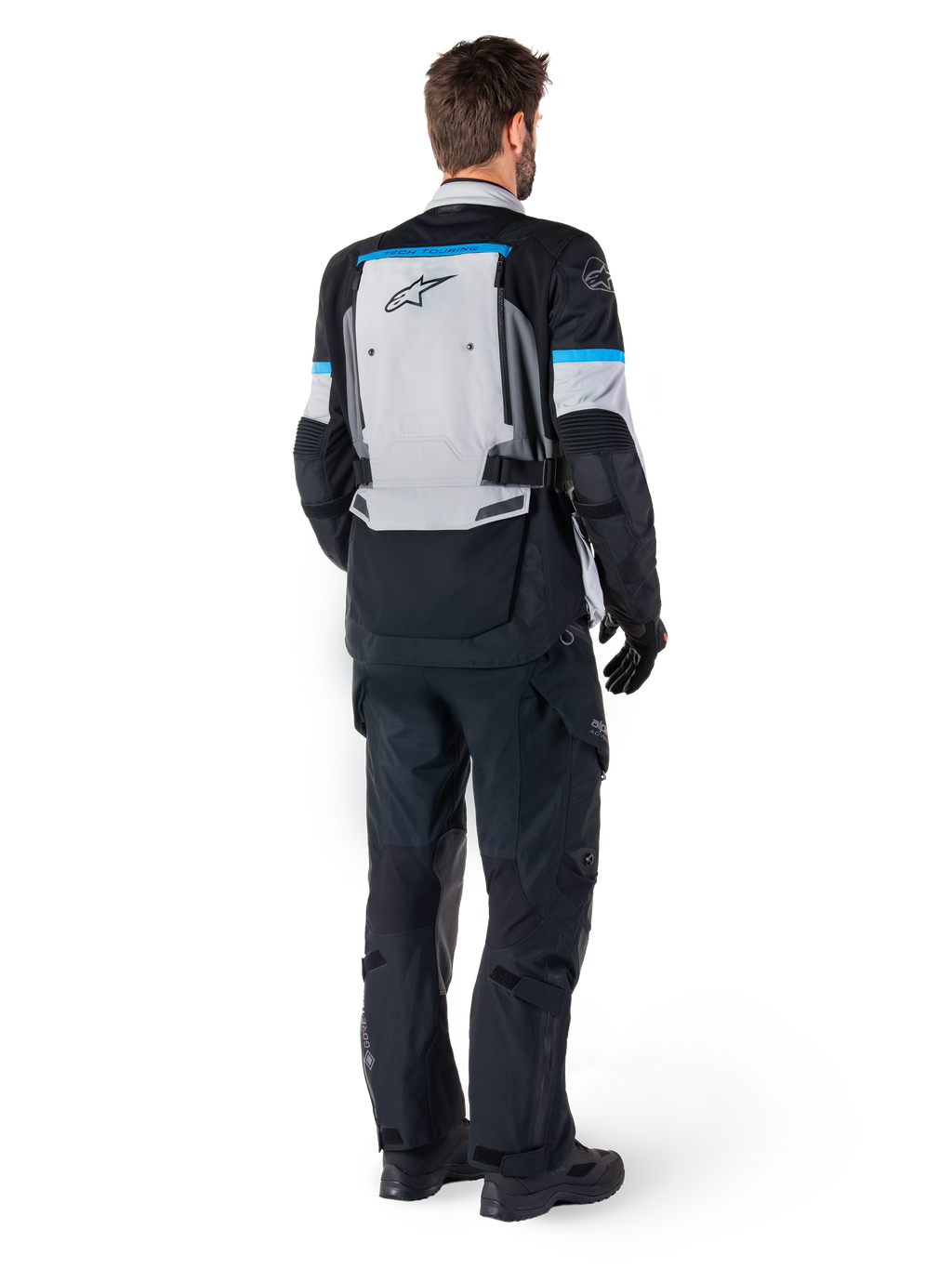 Alpinestars Bogota' Pro Drystar® jas, adventure motorjas, Ice Gray Black en Cyan, achteraanzicht gedragen met bijpassende zwarte broek en handschoenen, voorzien van een groot grijs rugpaneel met zwart Alpinestars-logo en cyaanblauwe accenten.