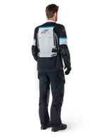 Alpinestars Bogota' Pro Drystar® jas, adventure motorjas, Ice Gray Black en Cyan, achteraanzicht gedragen met bijpassende zwarte broek en handschoenen, voorzien van een groot grijs rugpaneel met zwart Alpinestars-logo en cyaanblauwe accenten.