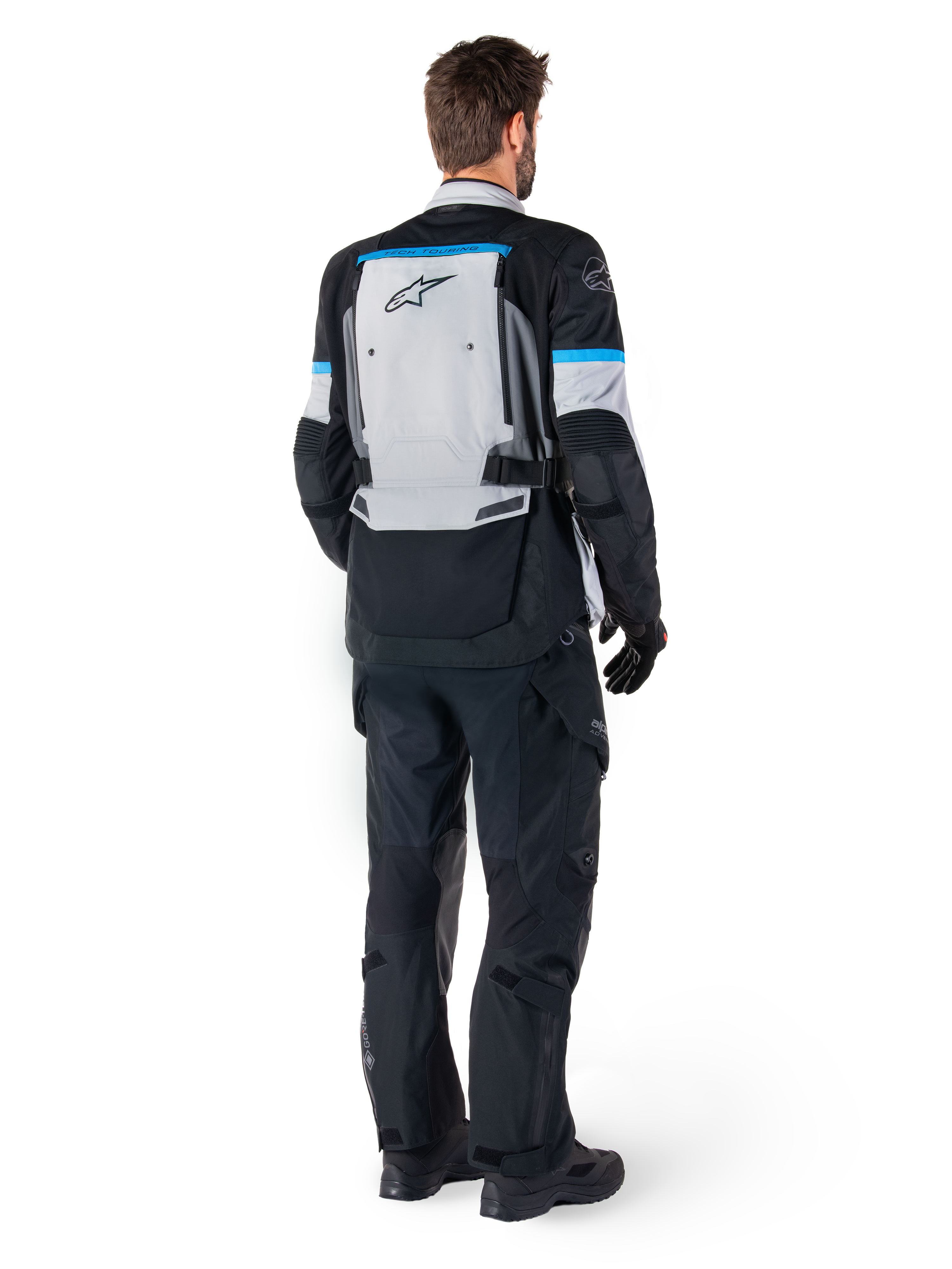 Alpinestars Bogota' Pro Drystar® jas, adventure motorjas, Ice Gray Black en Cyan, achteraanzicht gedragen met bijpassende zwarte broek en handschoenen, voorzien van een groot grijs rugpaneel met zwart Alpinestars-logo en cyaanblauwe accenten.