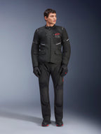 Mannelijk model in de Alpinestars Andes Air Drystar® Jas in het zwart, adventure touring motoruitrusting met bijpassende broek en handschoenen, voorzien van een rood logo op de borst, mesh-ventilatie en functionele zakken.