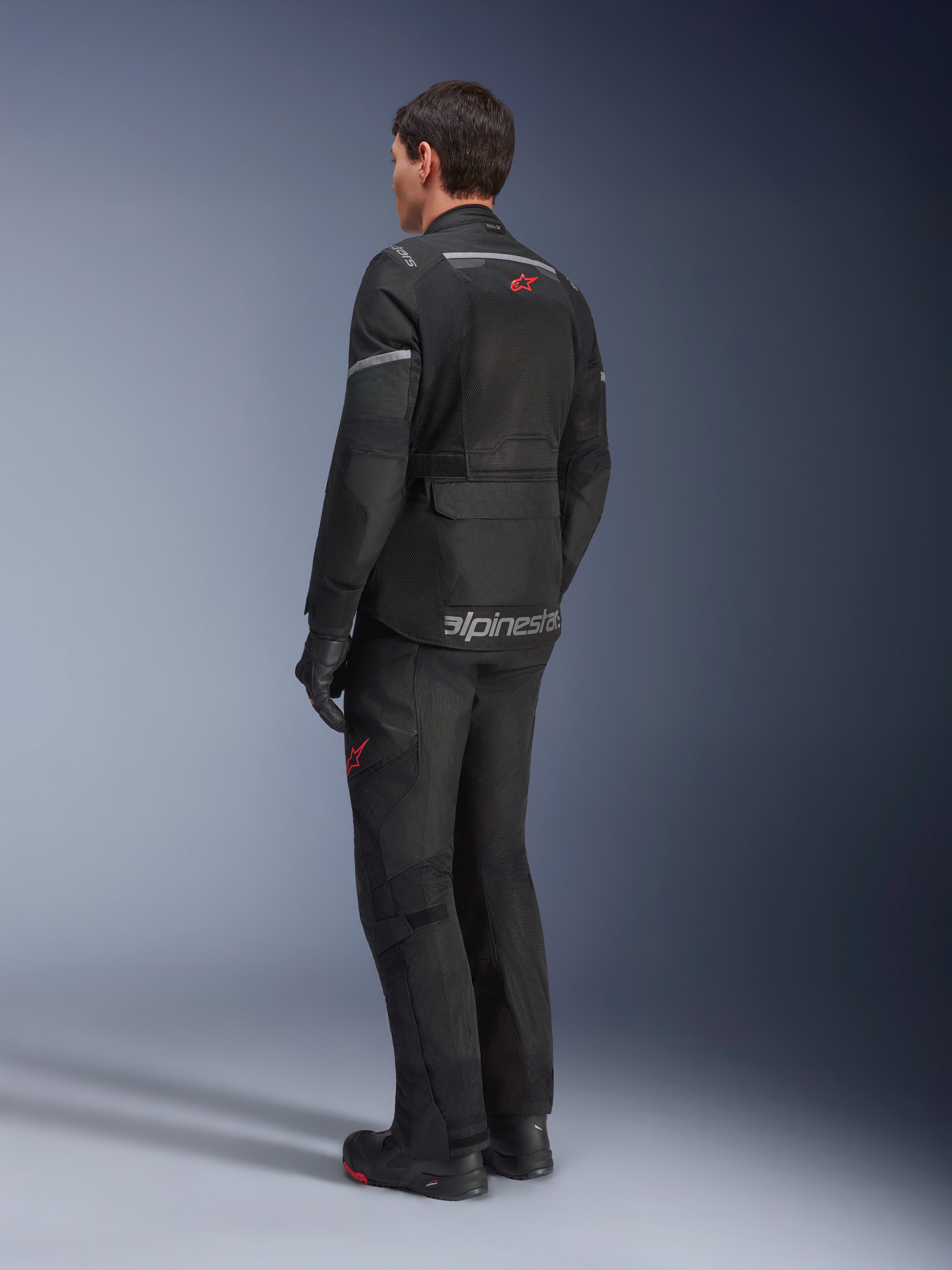Alpinestars Andes Air Drystar® Jas, zwart, achteraanzicht op een motorrijder, met uitgebreide mesh-panelen voor ventilatie, gedragen met bijpassende adventure motorbroek en laarzen, toont het weggeoriënteerde touring-ontwerp en de branding.