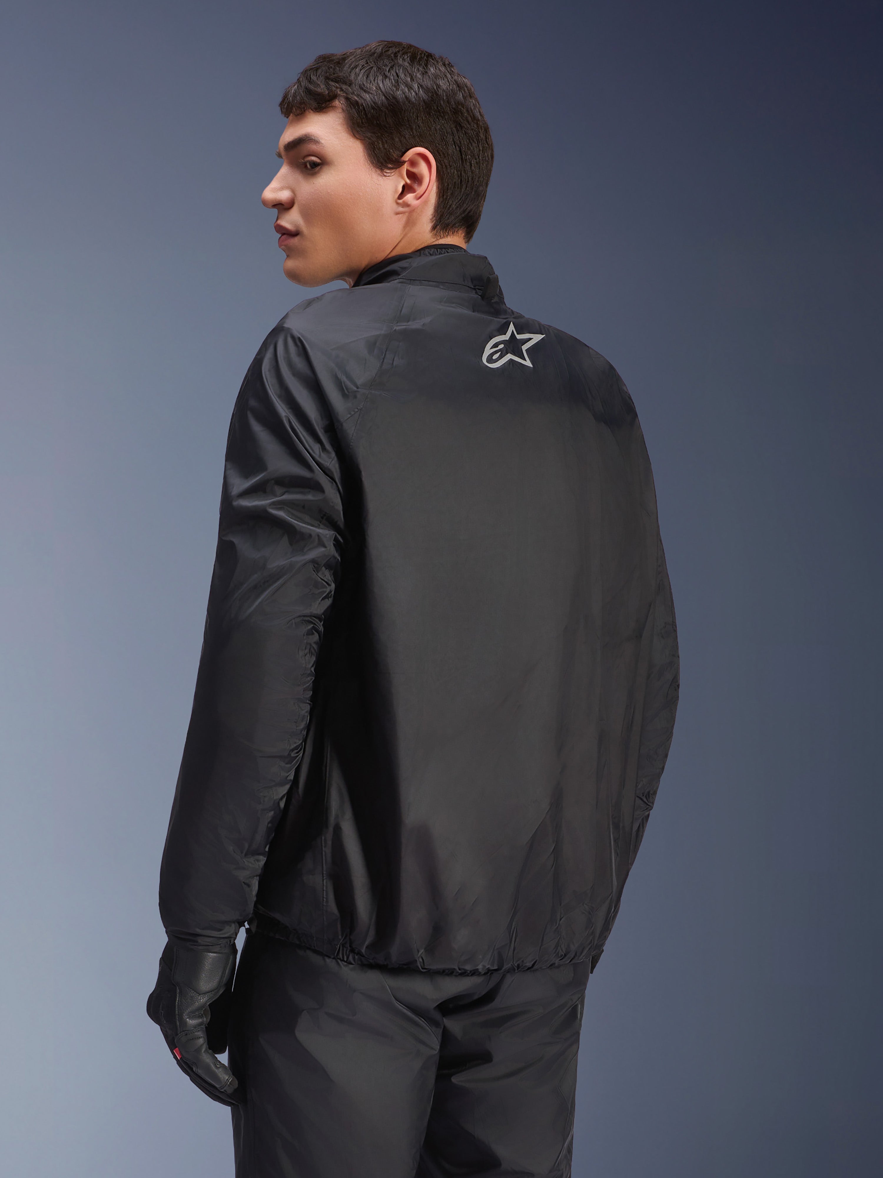 Alpinestars Andes Air Drystar® Jas, afneembaar waterdicht membraan in het zwart, achteraanzicht op een mannelijk model, met een klein wit Alpinestars-logo op de bovenrug, gecombineerd met zwarte motorhandschoenen