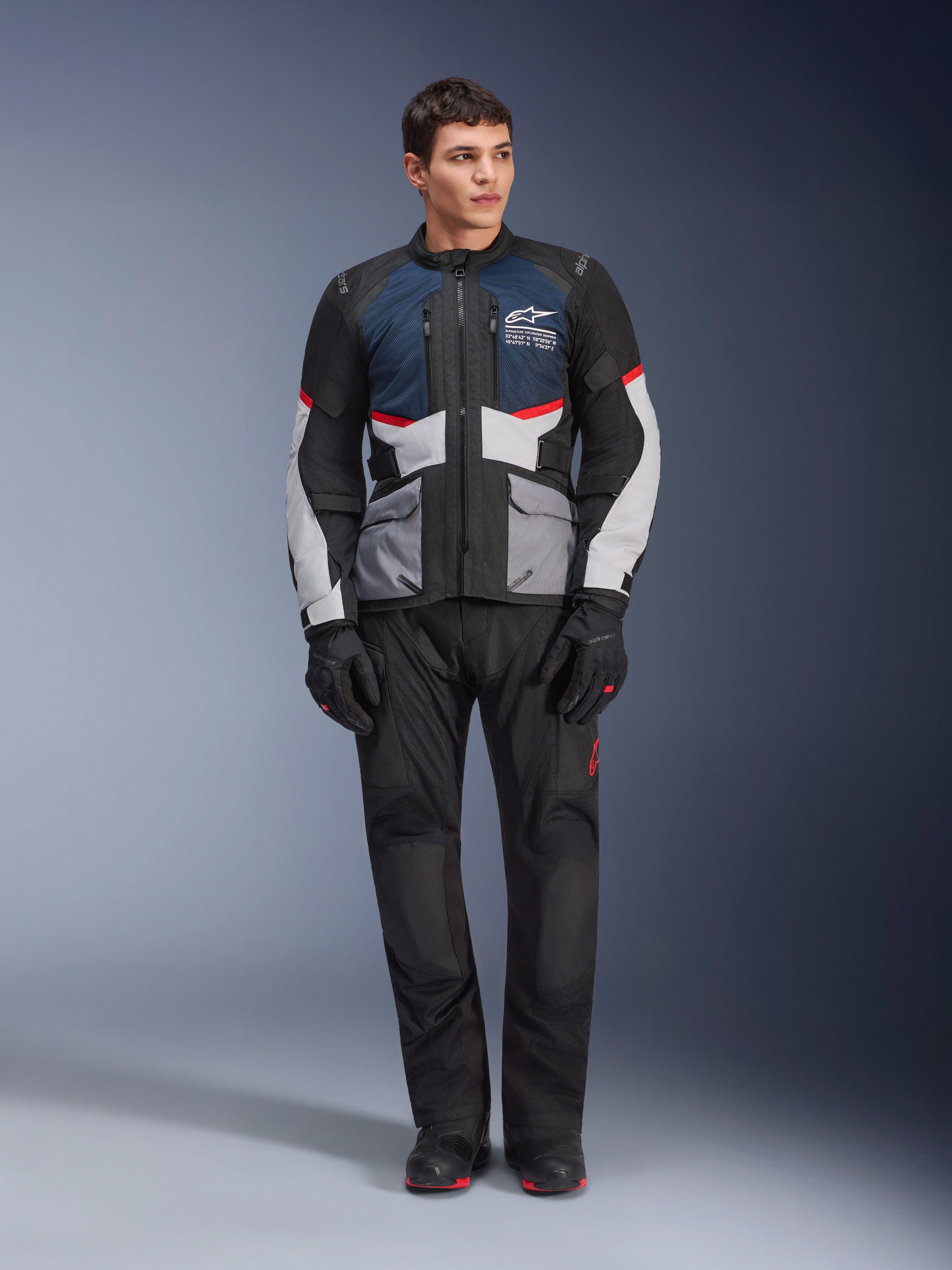 Alpinestars Andes Air Drystar® Jas, motortouringjas, Deep Blue Black en Ice Gray, gedragen met bijpassende zwarte adventure-broek en handschoenen, voorzien van mesh-panelen voor luchtstroom en een technisch ontwerp met meerdere zakken.