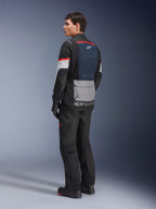 Mannelijk model van achteren en opzij gezien, dragend de Alpinestars Andes Air Drystar® Jas in Deep Blue Black Ice Gray, gecombineerd met een zwarte motorbroek en handschoenen, voorzien van een blauw mesh achterpaneel, grijze opbergzak op de onderrug en rode accenten op de mouwen, professionele adventure touring uitrusting.