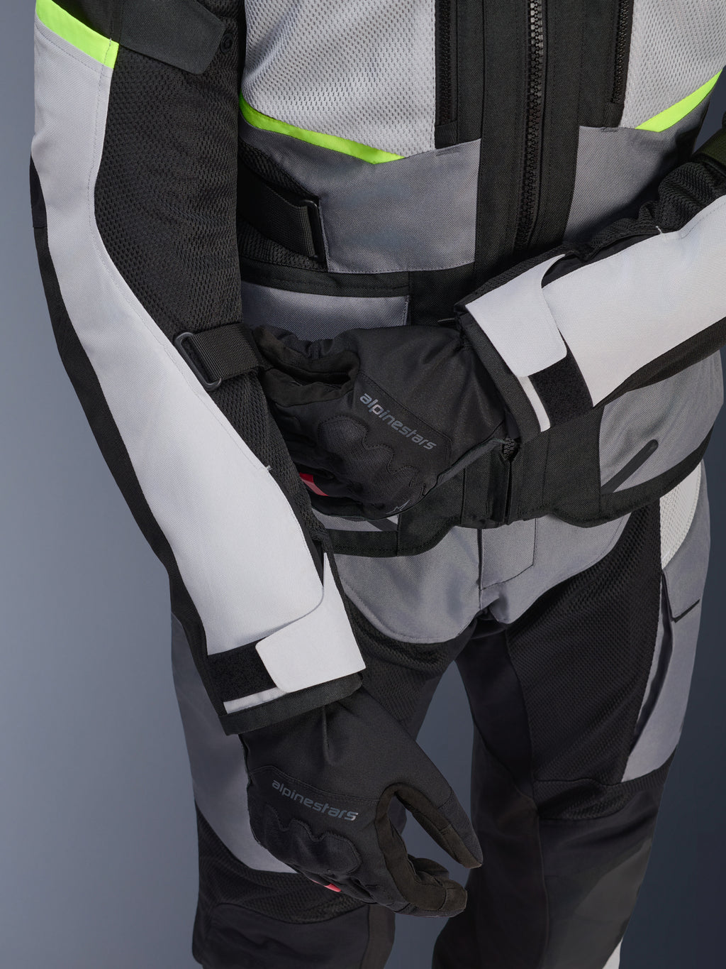 Alpinestars Andes Air Drystar® jas, motor-touringjas, ijsgrijs en donkergrijs met neongele accenten, close-up van meshpanelen en verstelbanden, gedragen met zwarte Alpinestars handschoenen