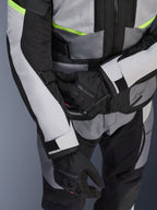 Alpinestars Andes Air Drystar® jas, motor-touringjas, ijsgrijs en donkergrijs met neongele accenten, close-up van meshpanelen en verstelbanden, gedragen met zwarte Alpinestars handschoenen
