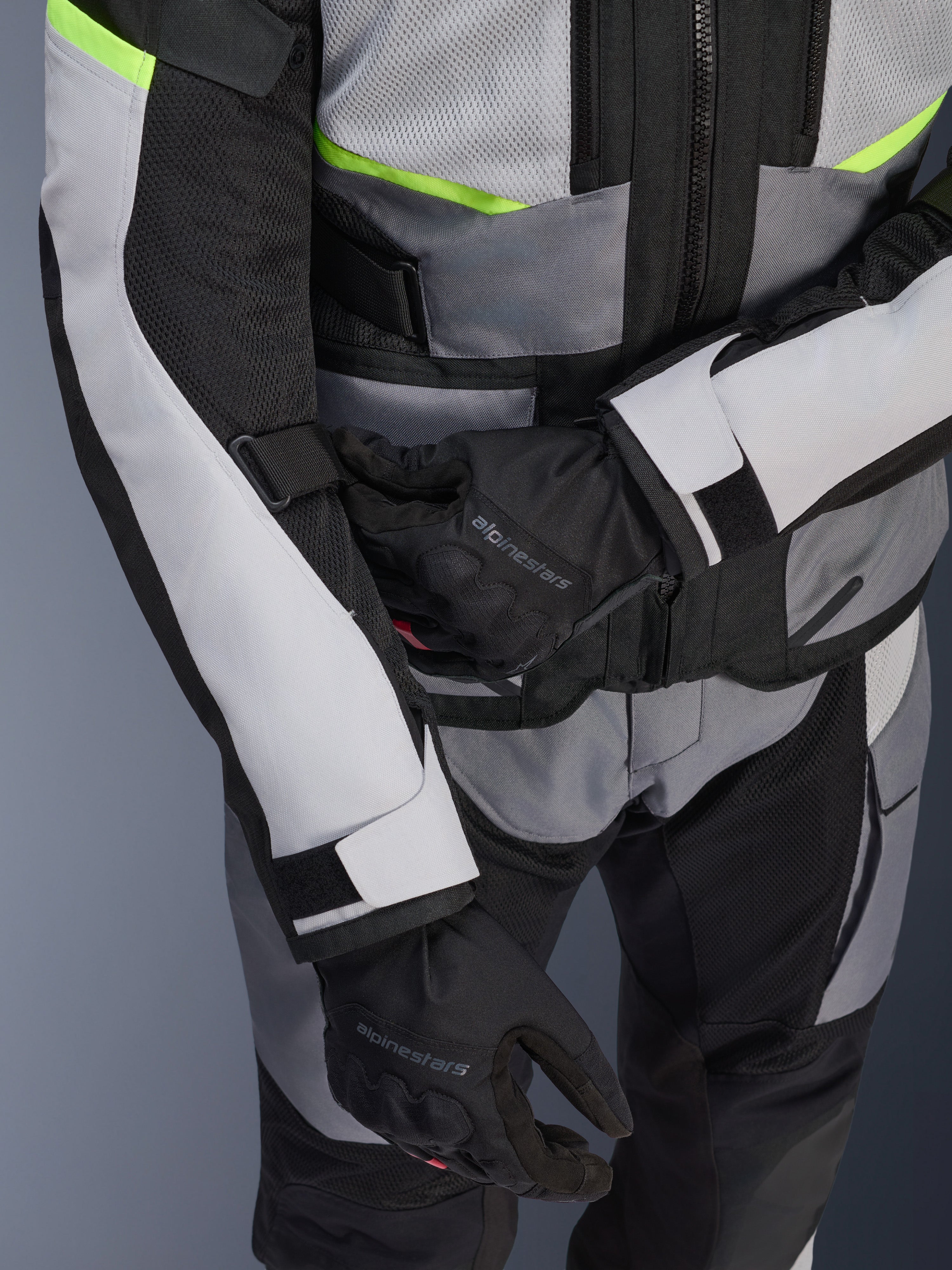 Alpinestars Andes Air Drystar® jas, motor-touringjas, ijsgrijs en donkergrijs met neongele accenten, close-up van meshpanelen en verstelbanden, gedragen met zwarte Alpinestars handschoenen
