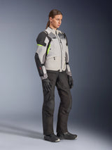 Alpinestars Woman Stella Andes V4 Drystar® Jacket, Ice Gray Dark Gray and Black with Yellow Fluo accents, worn by a female model with black motorcycle pants and gloves, adventure touring protective gear for women