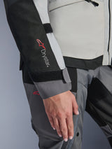 Close-up detail of the Alpinestars Woman Stella Andes V4 Drystar® Jacket, Ice Gray and Dark Gray, featuring the Drystar® branding on the black sleeve panel, adjustable velcro wrist closure, and durable adventure touring textile construction
