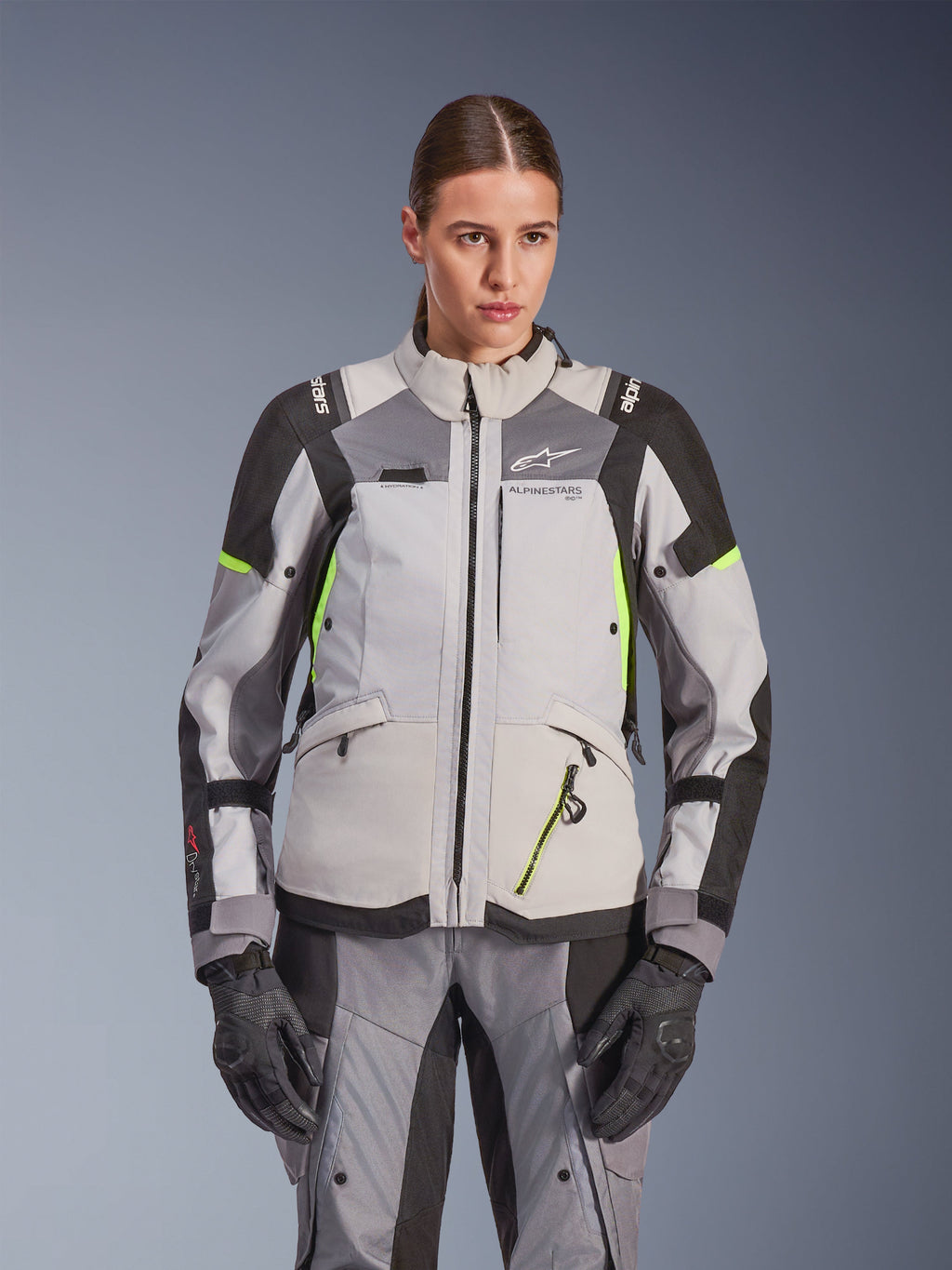 Alpinestars Stella Andes V4 Drystar® damesjas, adventure touring motorjas, Ice Gray en Dark Gray met Yellow Fluo accenten, gedragen met bijpassende broek en handschoenen, voorzien van beschermende textielconstructie en Alpinestars-branding.