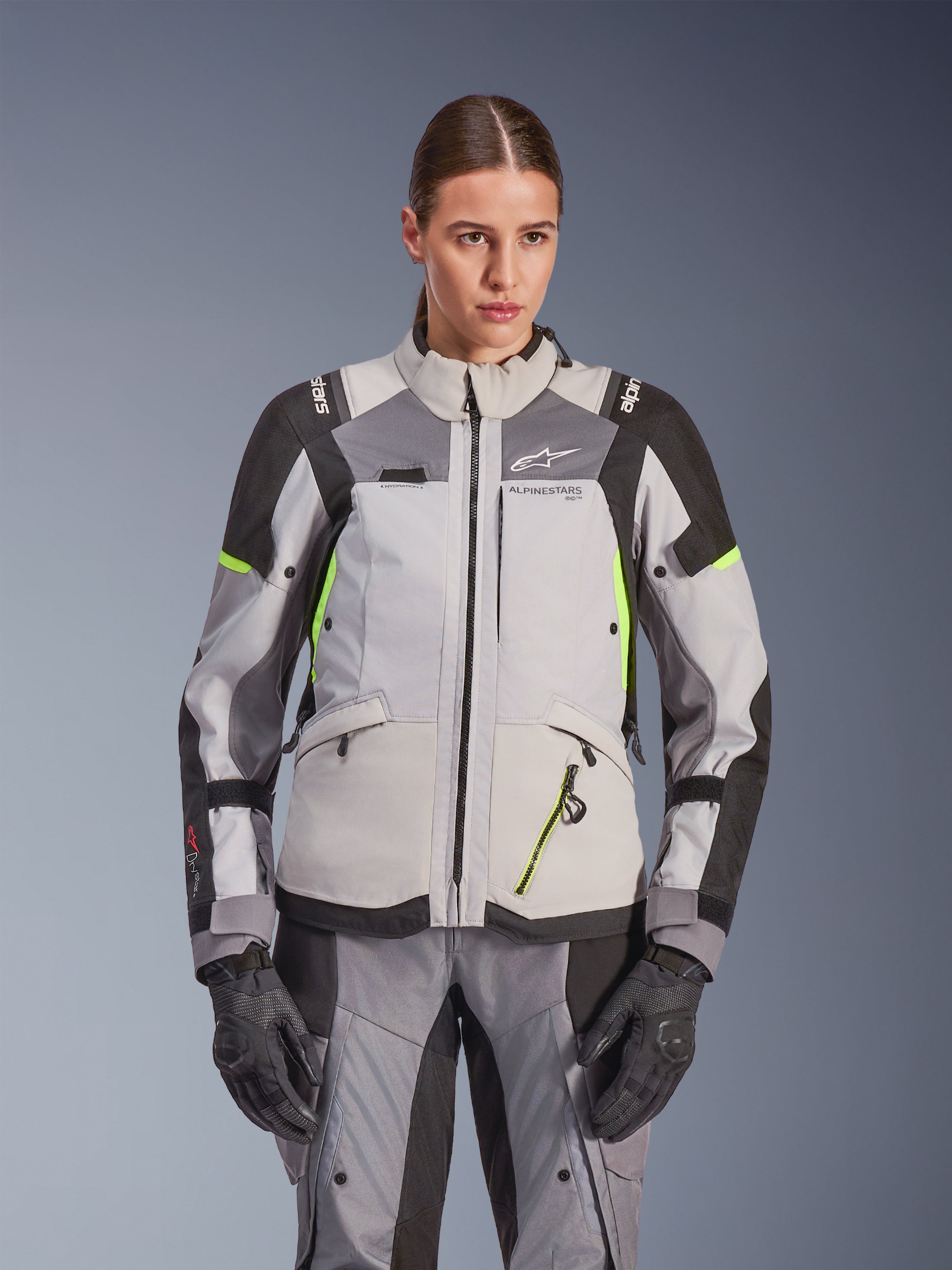 Alpinestars Stella Andes V4 Drystar® damesjas, adventure touring motorjas, Ice Gray en Dark Gray met Yellow Fluo accenten, gedragen met bijpassende broek en handschoenen, voorzien van beschermende textielconstructie en Alpinestars-branding.