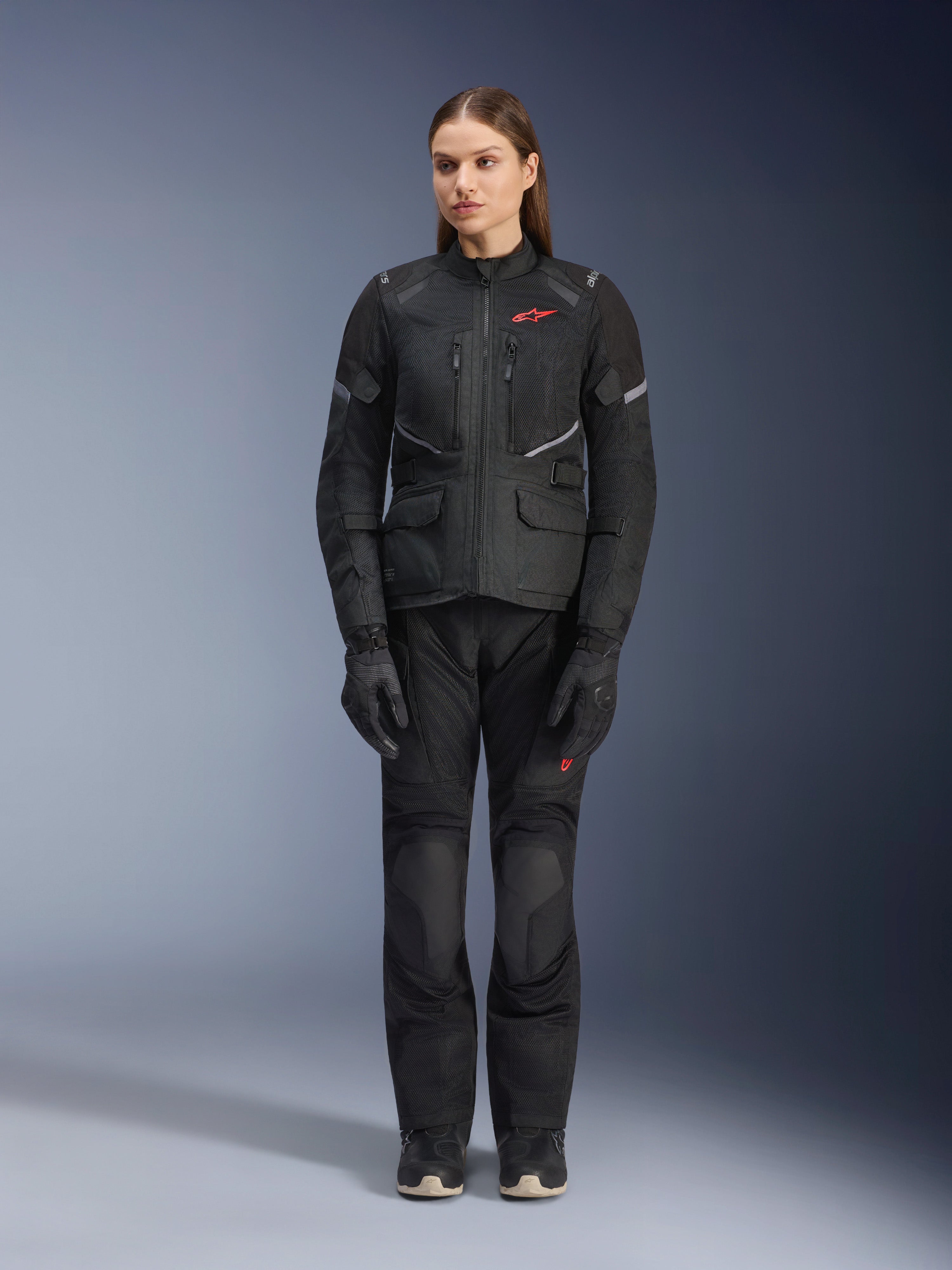 Female model wearing the Alpinestars Stella Andes Air Drystar® Jacket in Black, paired with matching black touring pants and gloves, featuring large mesh ventilation panels, red logo accents, and reflective details, professional studio shot for women's motorcycle gear.