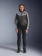 Vrouw in Alpinestars Stella T-Dyno WR-jas, zwart, donkergrijs en ecru, vooraanzicht, textiele motorjas met een op vintage geïnspireerd ontwerp, voorzien van merklogo's op de borst en mouwen, gedragen met een zwarte broek en laarzen