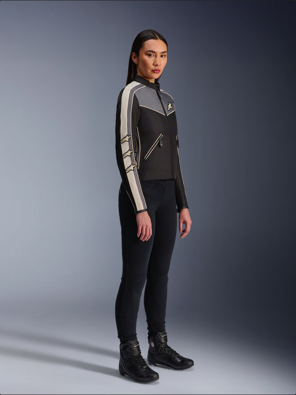 Alpinestars Stella T-Dyno WR Jas, textiele motorjas voor dames, zwart, donkergrijs en ecru, met een op vintage geïnspireerd ontwerp met crèmekleurige strepen op de mouwen en ster-logo's, gedragen met een zwarte broek en motorlaarzen, op erfgoed geïnspireerde urban motorkleding