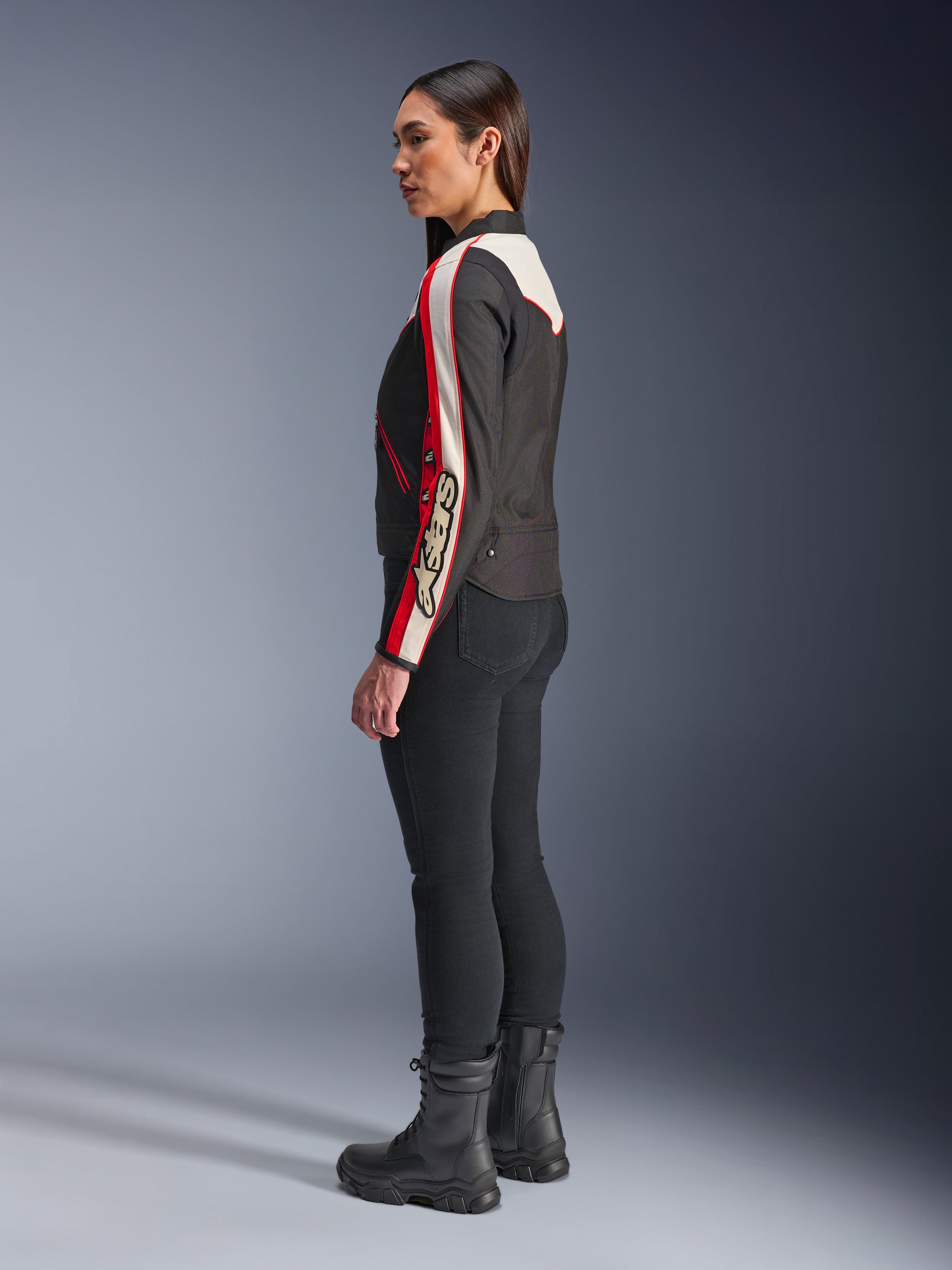 Alpinestars Stella T-Dyno WR Jas, textiele motorjas voor dames, zwart, ecru en helderrood, met een vintage-geïnspireerd ontwerp en Astars-branding op de mouw, gedragen met een slanke zwarte broek en zwarte laarzen, kortere biker-pasvorm voor stadsritten.
