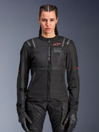 Alpinestars Stella ST-2 Air dames motorjas, zwart, vooraanzicht op model, voorzien van mesh panelen, rood logo op de borst en Alpinestars Exploration Equipment-branding, gedragen met zwarte handschoenen en een motorbroek