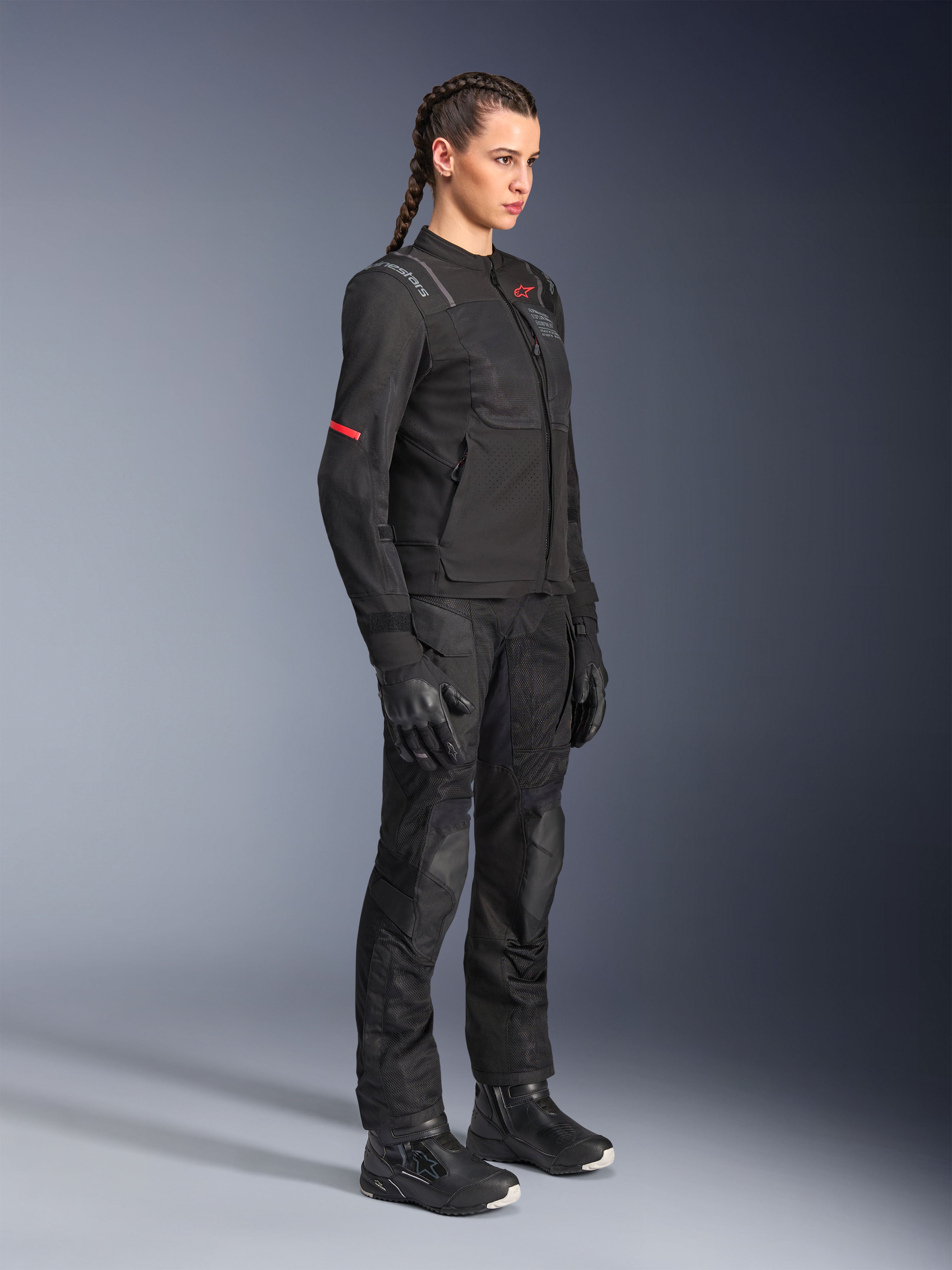 Vrouwelijk model in de Alpinestars Stella ST-2 Air Jacket in het zwart, gecombineerd met bijpassende zwarte motorbroek, handschoenen en laarzen, voorzien van mesh-ventilatiepanelen en subtiele rode details, strakke moderne touring-outfit