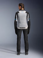 Alpinestars Stella ST-2 Air Jacket, Ice Gray Black, achteraanzicht op vrouwelijk model, voorzien van een groot lichtgrijs mesh rugpaneel, zwarte mouwen met blauwe streepaccenten, Alpinestars-branding op de onderrug, gecombineerd met zwarte technische motorbroek en laarzen, zomerse motoruitrusting