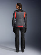 Achteraanzicht van een model dat de Alpinestars Stella St-2 Air damesjas draagt in Deep Gray en Dark Gray met Fluo Coral accenten, voorzien van grote mesh ventilatiepanelen op de rug en reflecterende logodetails, gecombineerd met een zwarte motorbroek en handschoenen.