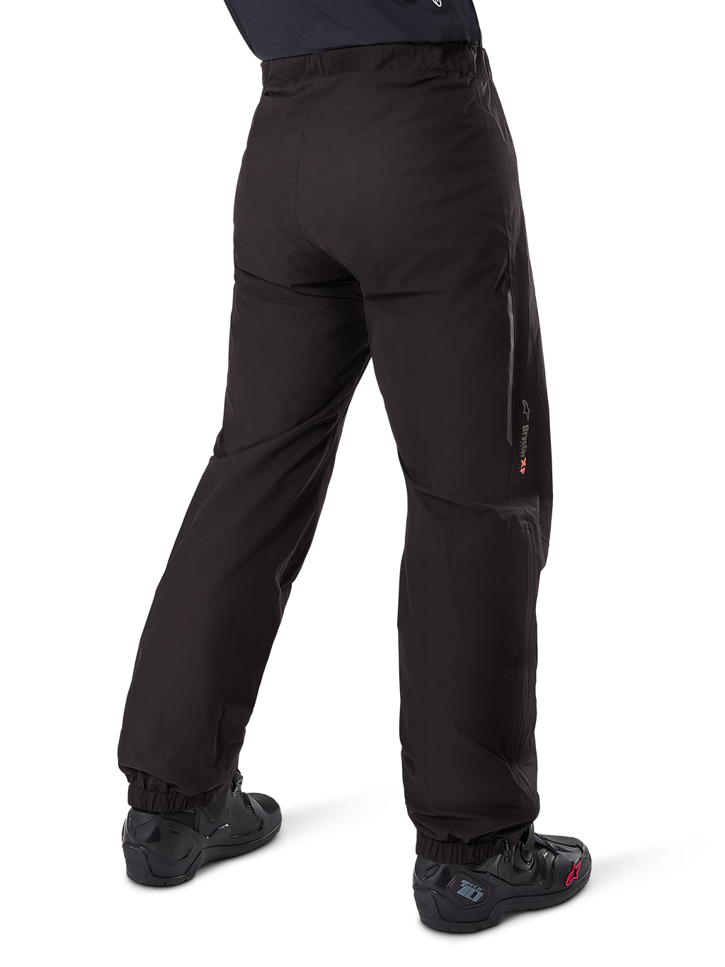 Alpinestars Amt-8 Stretch Drystar® XF broekvoering, zwart, achteraanzicht van de waterdichte voering gedragen over zwarte motorlaarzen, voorzien van Drystar XF-branding op het onderbeen, elastische enkelboorden en lichtgewicht stretchmateriaal voor adventure-touring.