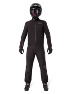 Motorrijder in Alpinestars AMT-8 Stretch Drystar® XF broekvoering en bijpassende jas, volledig zwarte waterdichte en winddichte technische uitrusting, met een zwarte helm, handschoenen en laarzen, strak adventure touring ontwerp.