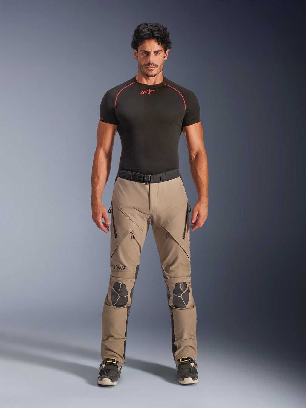Mannelijk model draagt Alpinestars AMT-8 Stretch Drystar® XF broek in Walnut en Black, gecombineerd met een zwarte basislaag met korte mouwen, adventure touring broek met verstevigde knieën, ventilatie met ritssluiting en ergonomisch stretch-ontwerp