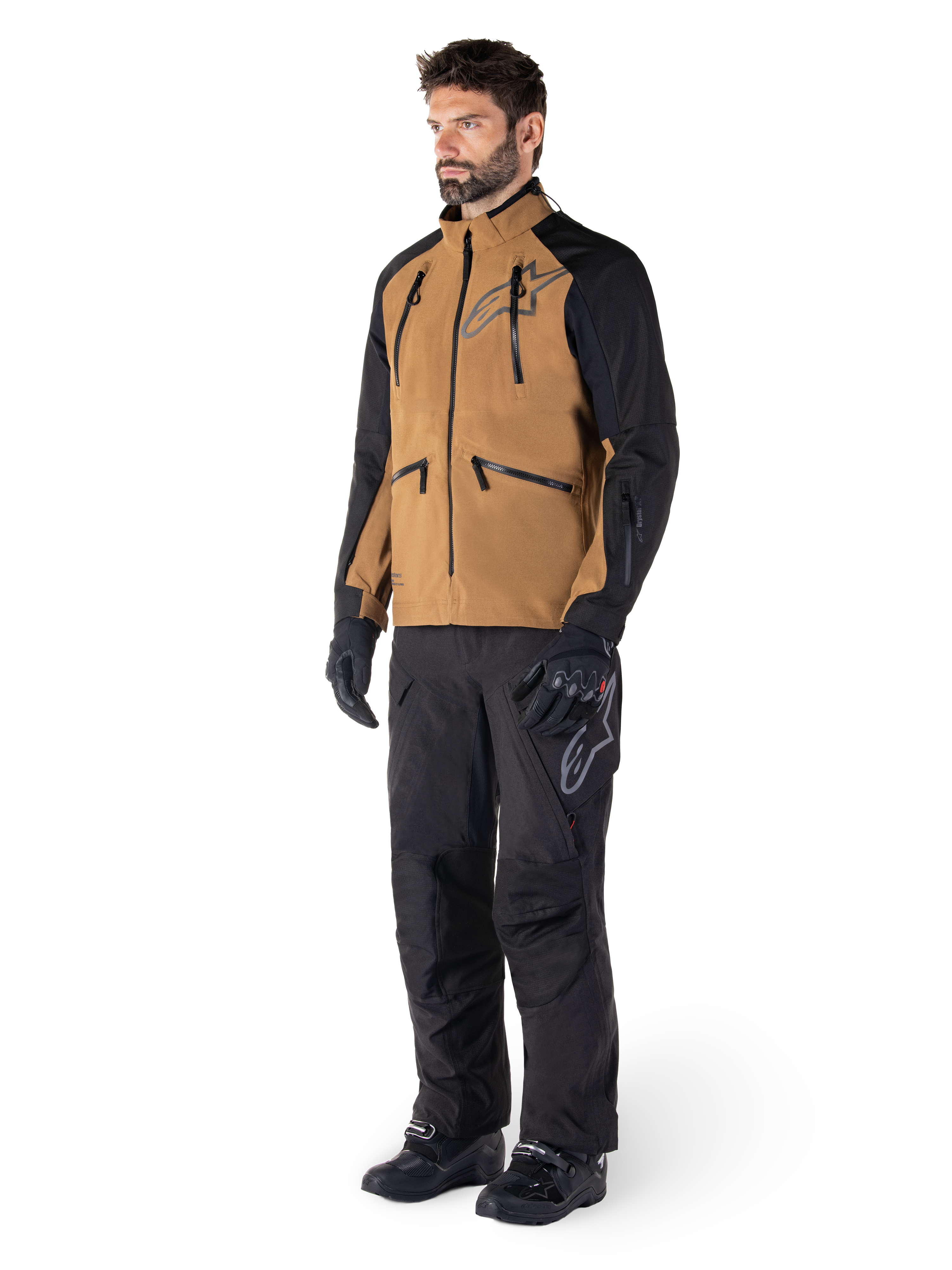 Alpinestars Hyde XT Drystar® broek, adventure motorbroek, zwart, gedragen met een bruine en zwarte technische jas, zwarte handschoenen en laarzen, met een over-de-laars ontwerp voor off-road en dual-sport rijden