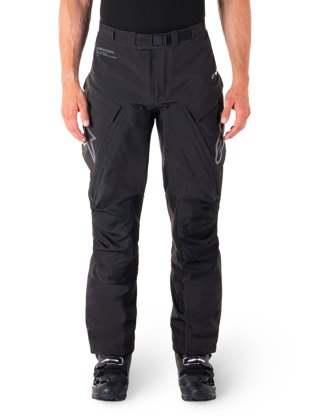Alpinestars Hyde XT Drystar broek, zwarte adventure touring motorbroek, gedragen door een rijder met zwarte laarzen, voorzien van grijze logo's op de dijen, geïntegreerde riem, versterkte kniepanelen en waterdichte textielconstructie