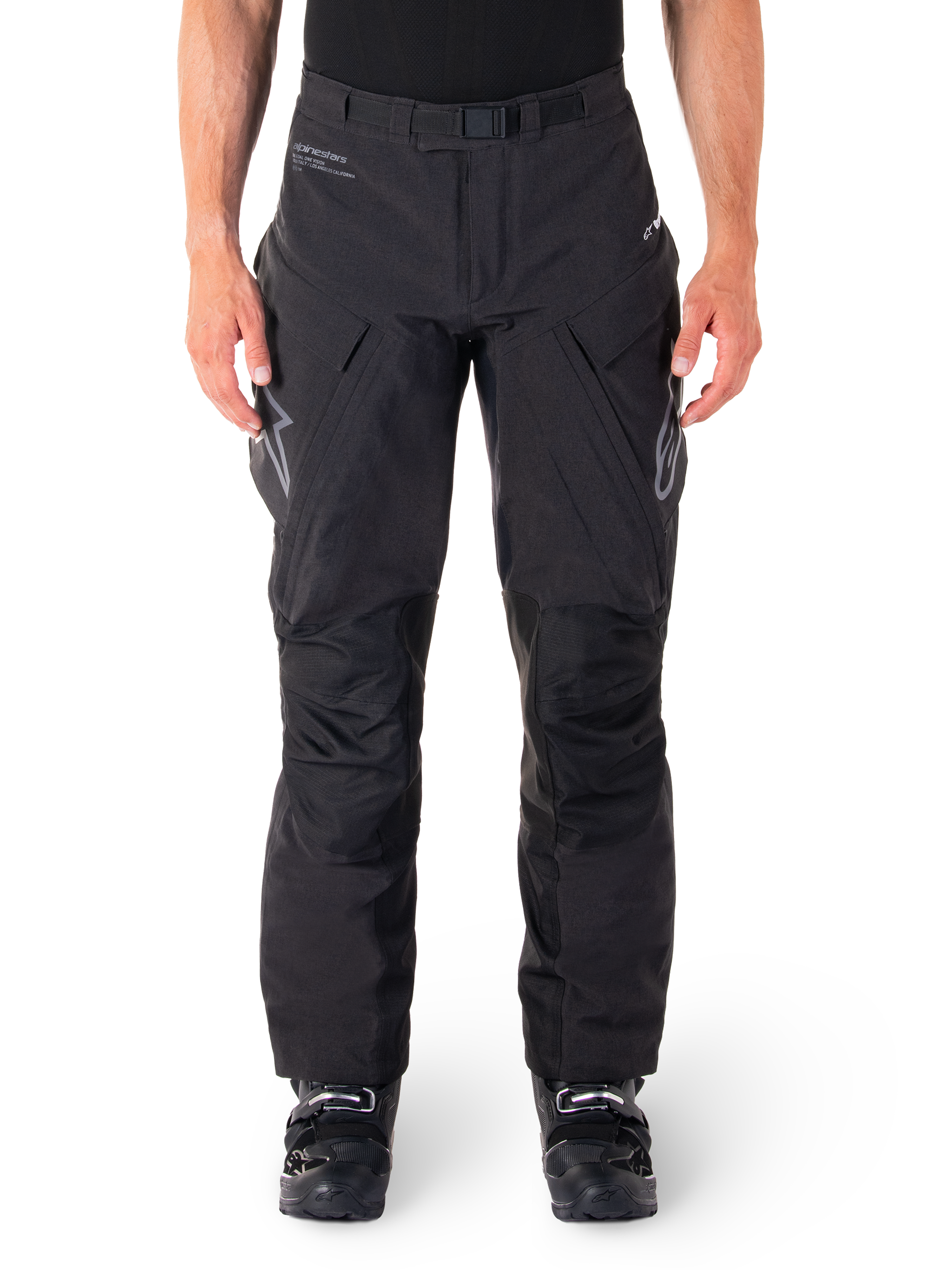 Alpinestars Hyde XT Drystar broek, zwarte adventure touring motorbroek, gedragen door een rijder met zwarte laarzen, voorzien van grijze logo's op de dijen, geïntegreerde riem, versterkte kniepanelen en waterdichte textielconstructie