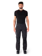 Alpinestars Hyde XT Drystar® Broek, adventure touring motorbroek, zwart, gedragen door een model met een zwarte basislaag met korte mouwen en zwarte laarzen, voorzien van technisch stretchmateriaal, versterkte kniepanelen en ergonomische cargozakken.
