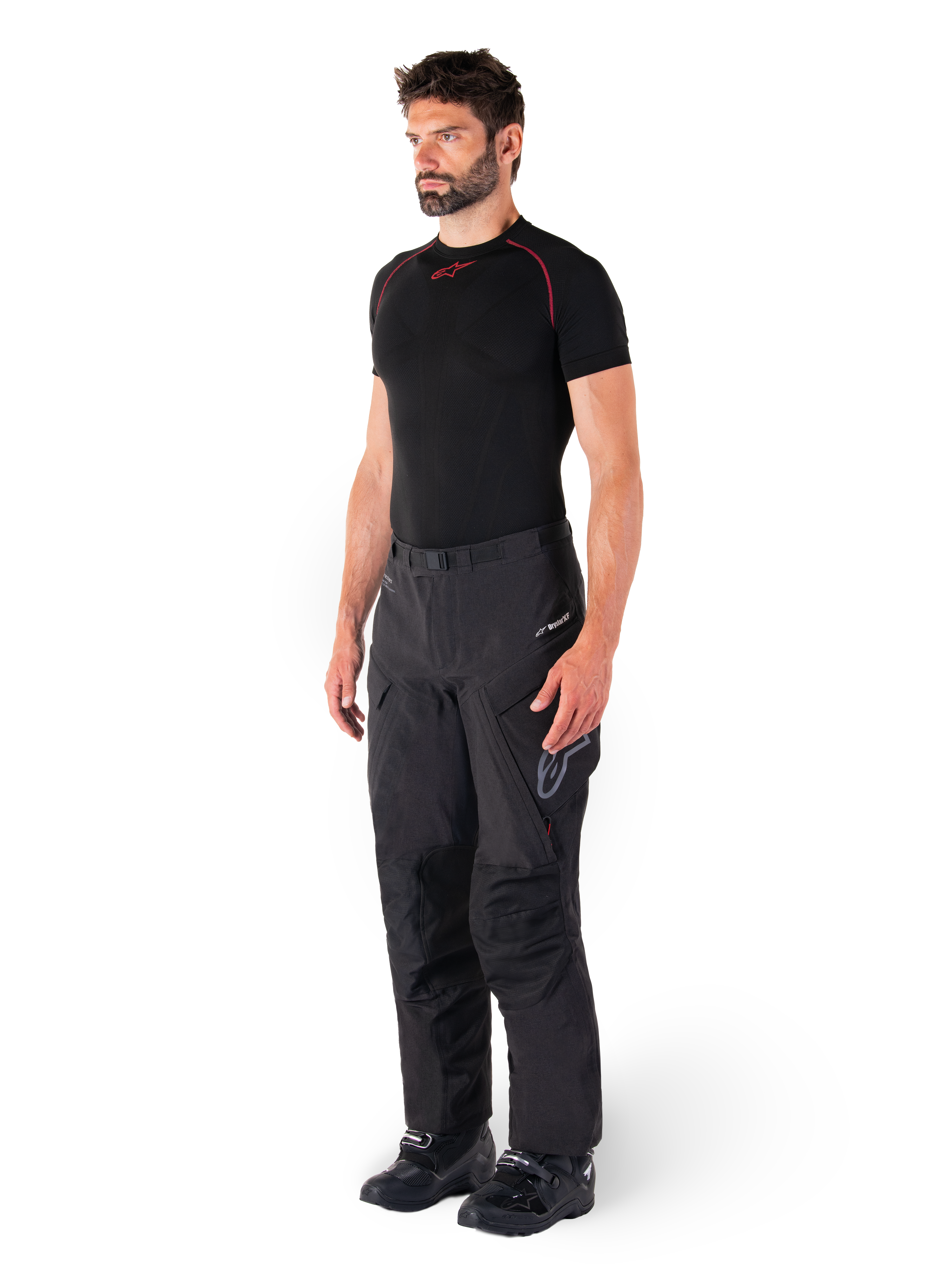 Alpinestars Hyde XT Drystar® broek, zwarte adventure touring motorbroek gedragen door een model met een zwart compressieshirt en zwarte laarzen, voorzien van een technische waterdichte constructie en Drystar®XF-branding.