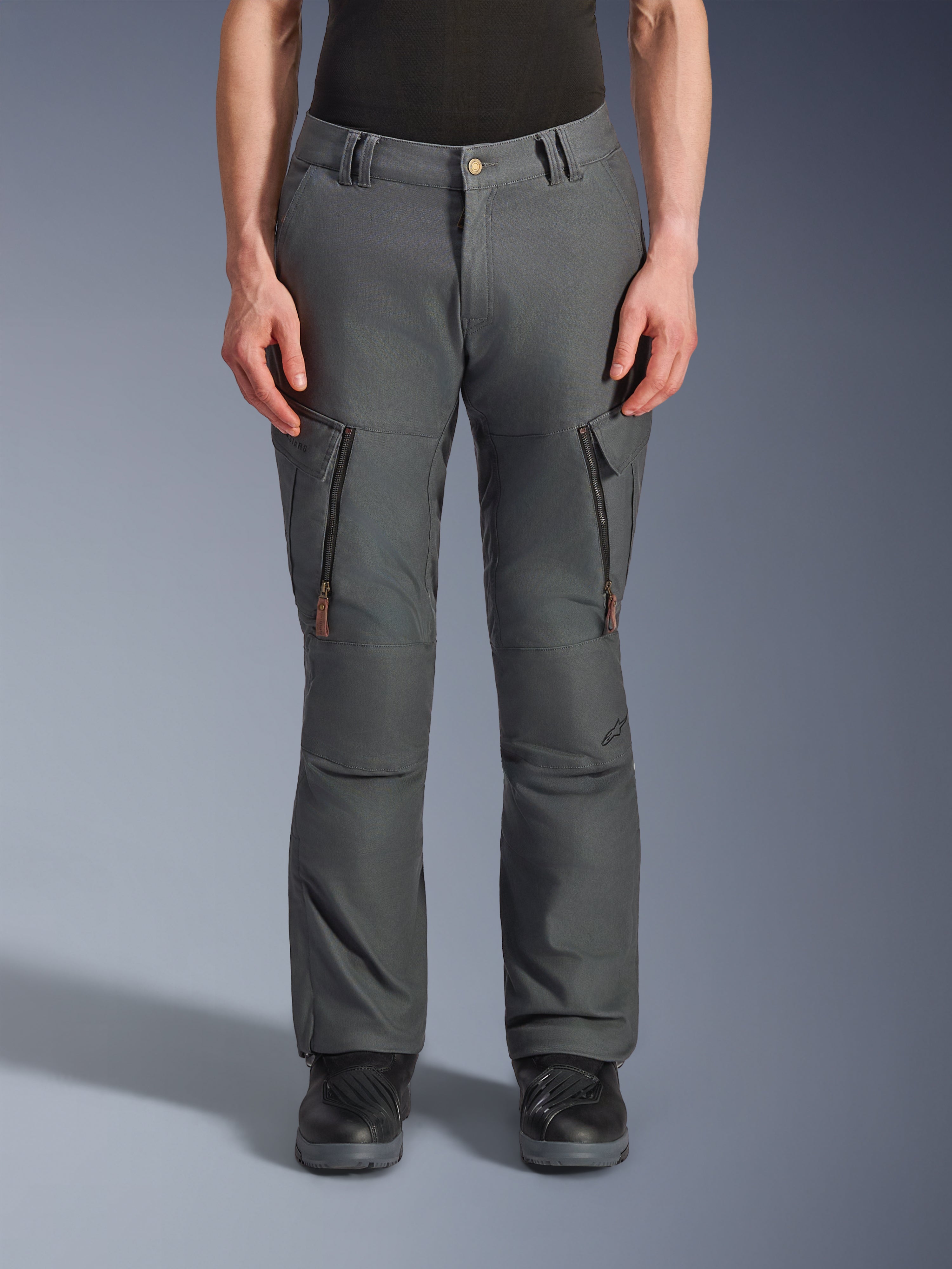 Alpinestars Borrego Drystar® broek, avontuurlijke motorbroek, antracietgrijs, met verticale ritszakken op de dijen met leren lipjes, knoopsluiting en riemlussen, gedragen door een model met zwarte motorlaarzen