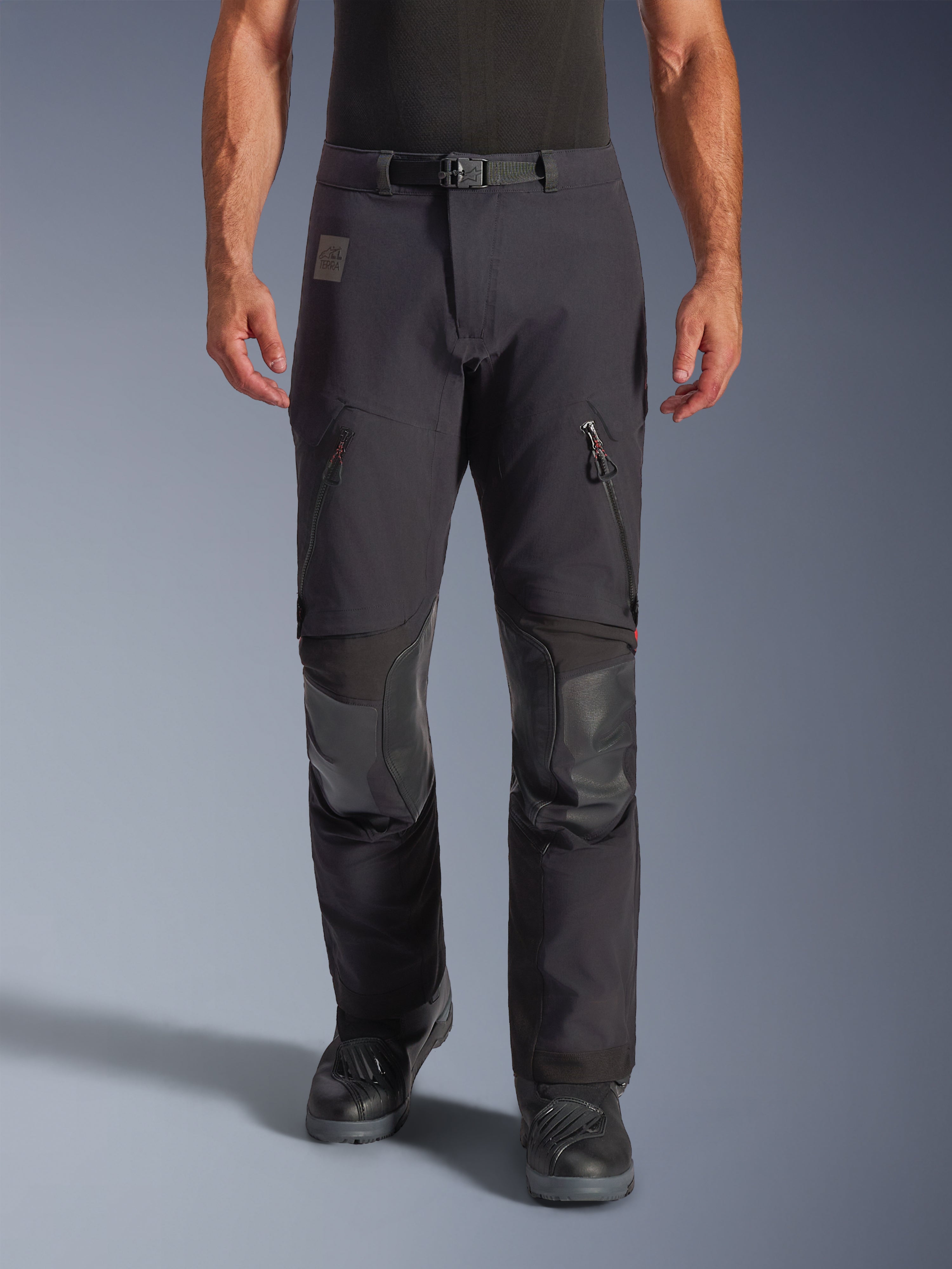 Alpinestars Halo Pro Drystar® XF gelamineerde broek in Black Dark Shadow, adventure motorbroek, vooraanzicht op model met magnetische taille-gesp, ventilatieopeningen op de dijen met rits en versterkte lederen kniestukken, gecombineerd met zwarte motorlaarzen.