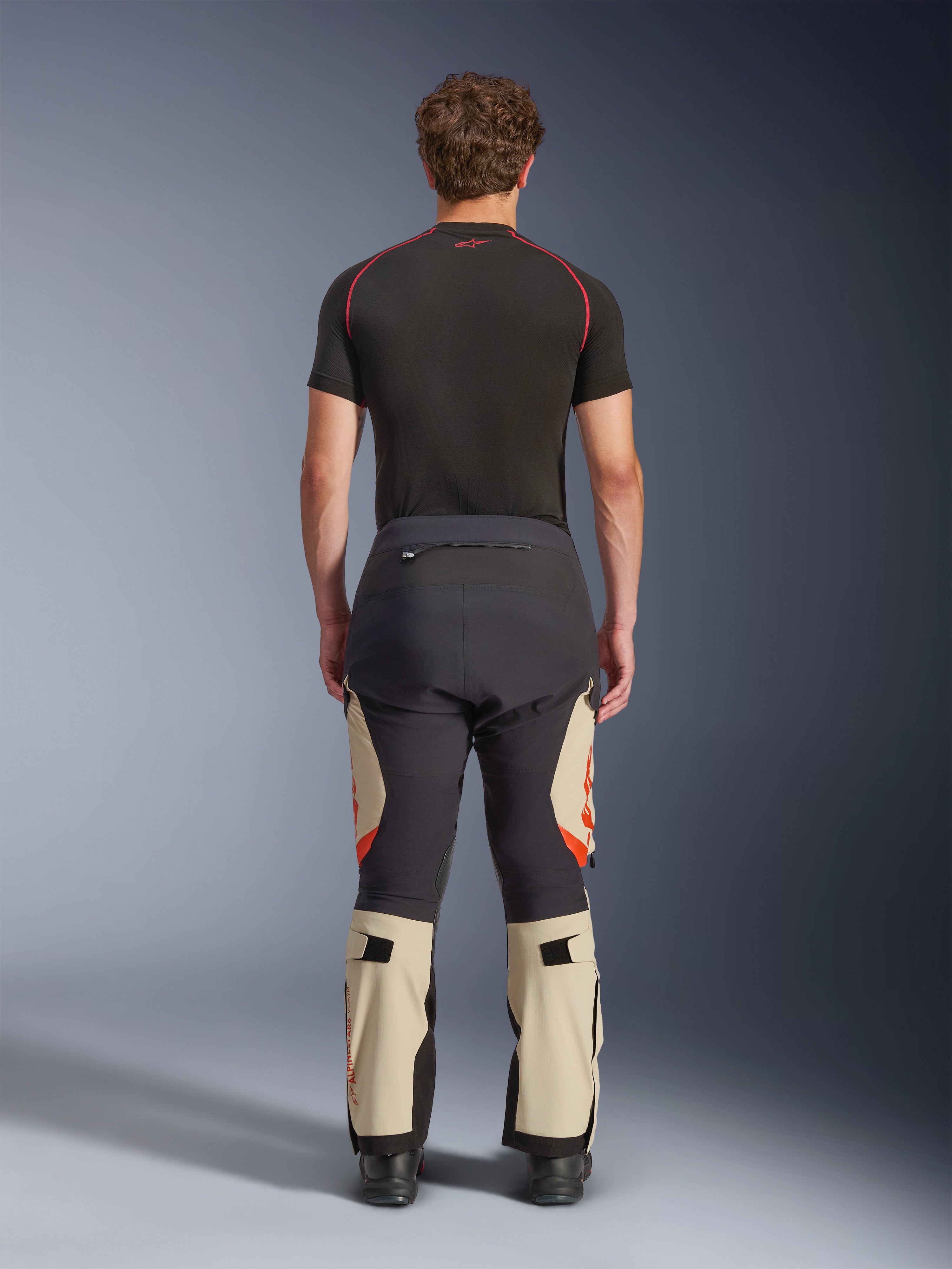 Alpinestars Halo Pro Drystar® XF Laminated Pants, Mastic Black, rear view on a model, black and beige color blocking with orange logos, adventure motorcycle touring pants with durable textile construction and adjustable calf sections