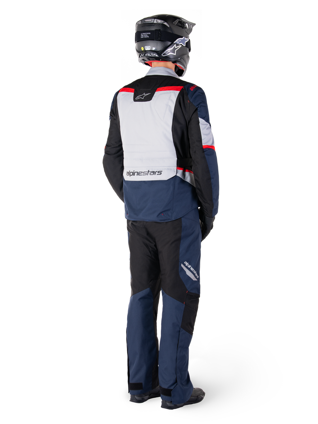 Achteraanzicht van een motorrijder in Alpinestars ST-1 Waterproof broek en bijpassend jack in Dark Blue Black en Bright Red, adventure touring-uitrusting met textielpanelen en reflecterende accenten, gecombineerd met een zwarte helm en laarzen