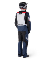 Achteraanzicht van een motorrijder in Alpinestars ST-1 Waterproof broek en bijpassend jack in Dark Blue Black en Bright Red, adventure touring-uitrusting met textielpanelen en reflecterende accenten, gecombineerd met een zwarte helm en laarzen